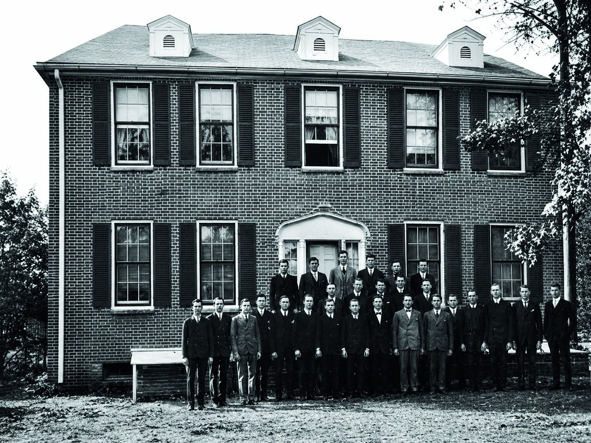 An archival black-and-white photograph of members in front of the original brick Beta house at Ole Miss